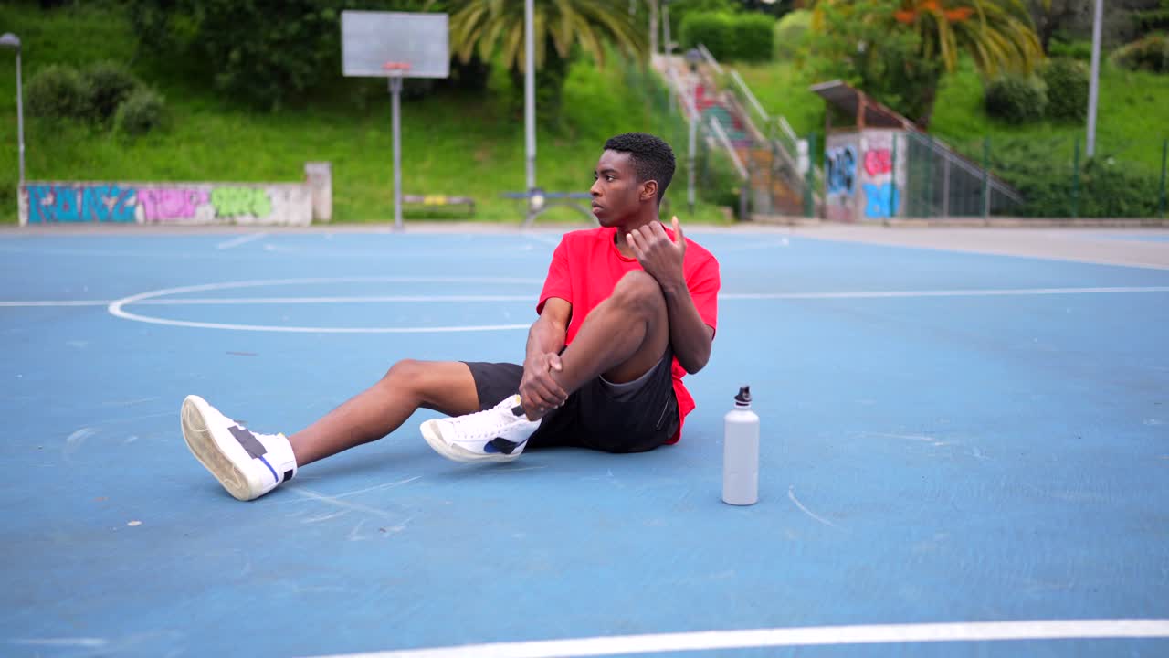 Giovane uomo a riposo su un campo da basket con borraccia