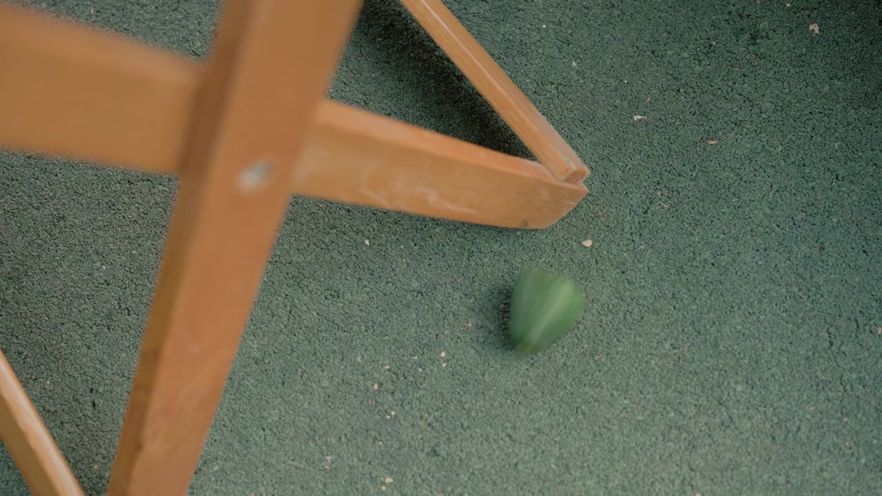 Wooden chair leg moves slowly across green textured floor revealing interaction between furniture and flooring material. consistent motion highlights details of both wood grain texture