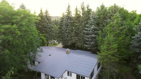 Aerial-pedestal-up-shot-of-a-cabin-tucked-into-the-woods-then-revealing-a-bright-sunny-forest-and-sky-at-sunset