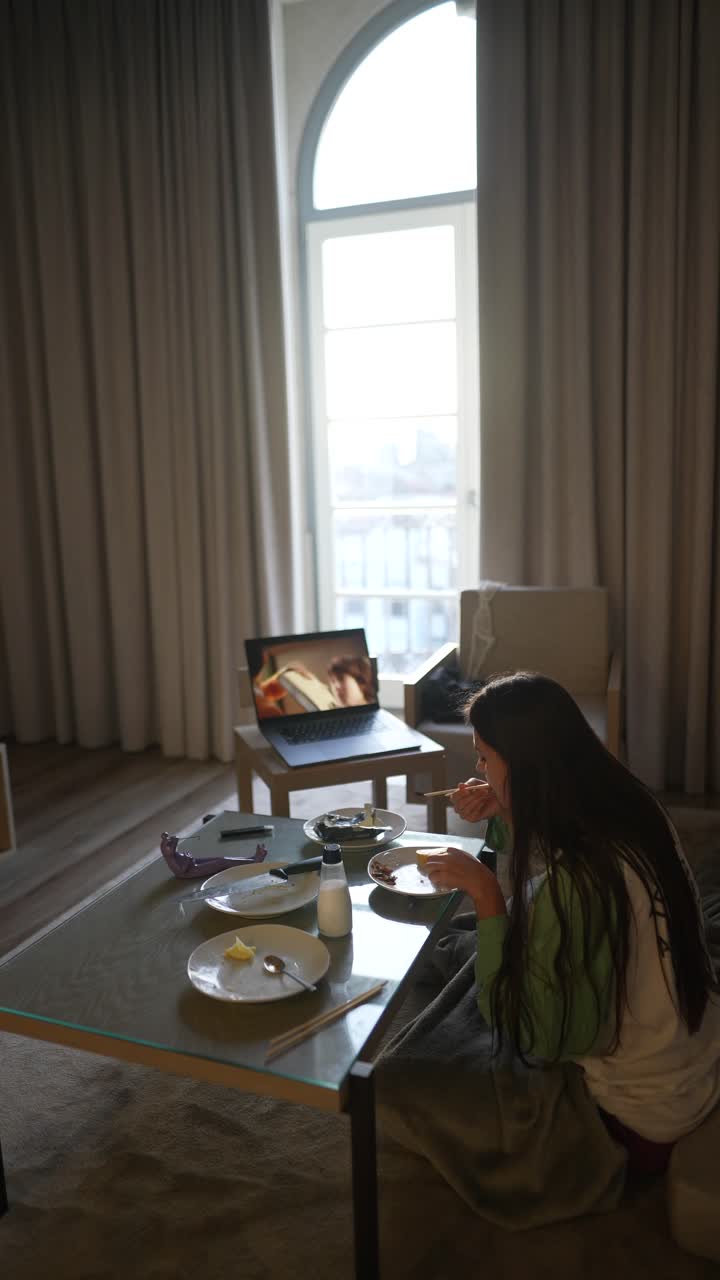 여자애가 비디오 통화 중에 호텔 방에서 먹고 있다.