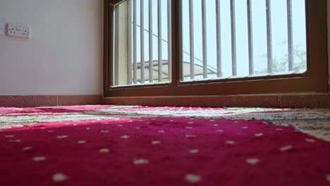 barefoot man walks slowly on a red prayer rug in a sunlit room. peaceful domestic moment. perfect for themes of mindfulness, culture, calm mornings, or home living.