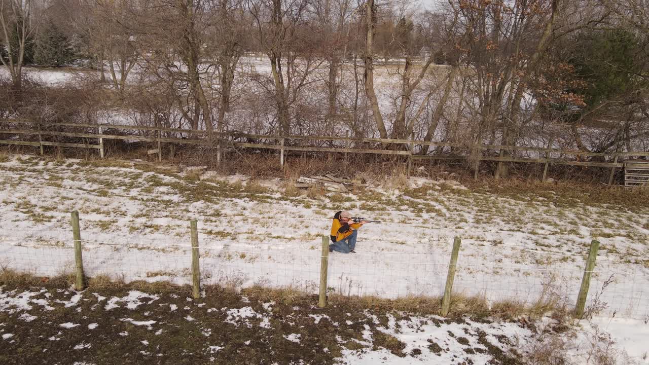 Man with rifle walking and ducking before shooting, aerial follow view