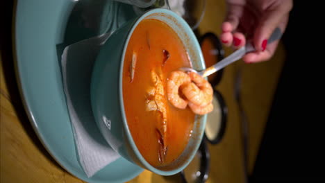 Cámara-Lenta-Vertical-De-Una-Mano-Femenina-Sosteniendo-Camarones-Con-Una-Cuchara-De-Una-Sopa-Roja-De-Mariscos-Con-Un-Cangrejo-En-Un-Tazón-Azul