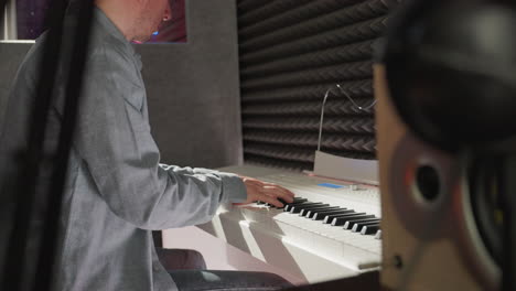 a focused man in a long sleeve shirt sits at a white piano in a studio with a black background, reflecting a mix of creativity and professionalism. the scene is lit to enhance the artistic atmosphere