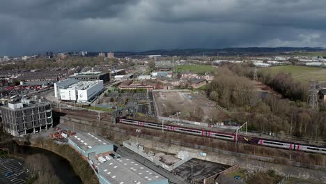 Aerial-footage-of-trains-approaching-Stoke-on-Trent-train-station-in-the-midlands-by-the-canal,-waterside-and-A50-motorway,-the-midway-point-for-commuters-who-travel-north-and-south-through-the-UK