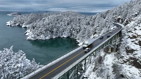 Vista-Aérea-De-Un-Semi-Camión-Blanco-Que-Viaja-Sobre-Un-Puente-Cubierto-De-Nieve-Para-Entregar-Su-Envío