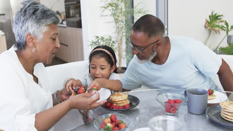 Niña-Birracial-Disfruta-Del-Desayuno-Con-Sus-Abuelos,-Una-Mujer-Y-Un-Hombre-Birraciales