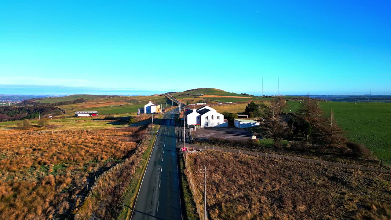imágenes de video de drones aéreos que se mueven lentamente por una carretera rural y pasan por edificios encalados, en lo alto de las colinas pennine, reino unido