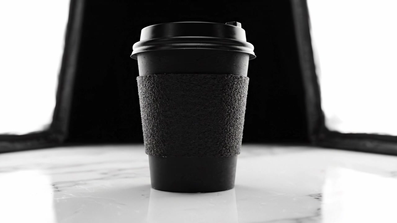 Tazza da caffè nera di design su superficie di marmo, circondata da morbido tessuto nero in stile minimalista, con focus su texture ed elementi di design.