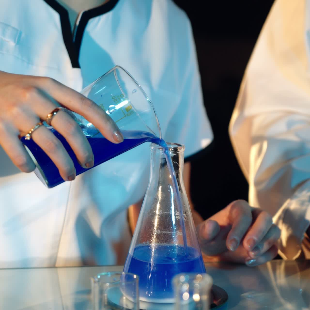 Chemists in goggles are considering the reaction of the substance in the tank on the table. A man and a woman are working on an experiment. Close-up