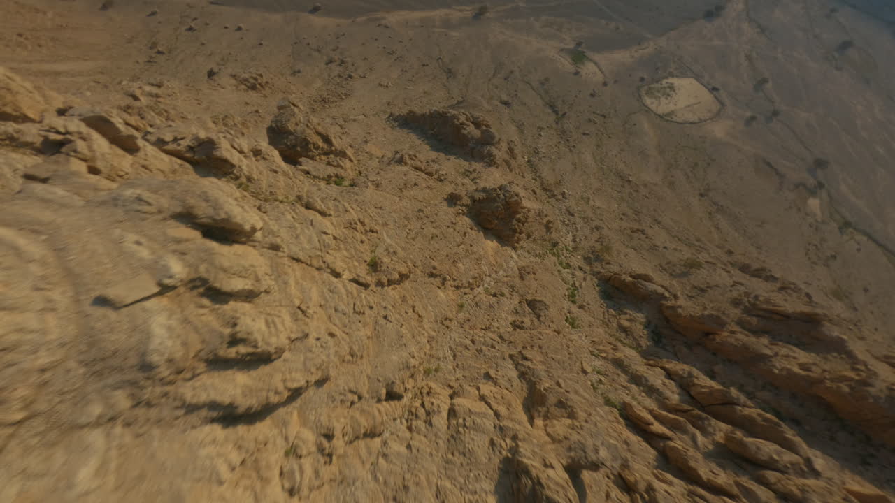 FPV drone dives steeply along rocky mountain slope, then tilts up and flies over desert road at sunset
