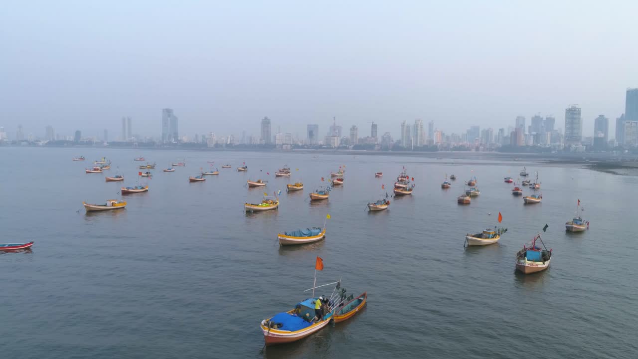 Volo laterale con le barche dei pescatori di Koliwada parcheggiate in primo piano e la vista della città di Mumbai sullo sfondo sotto un cielo fosco simile allo smog