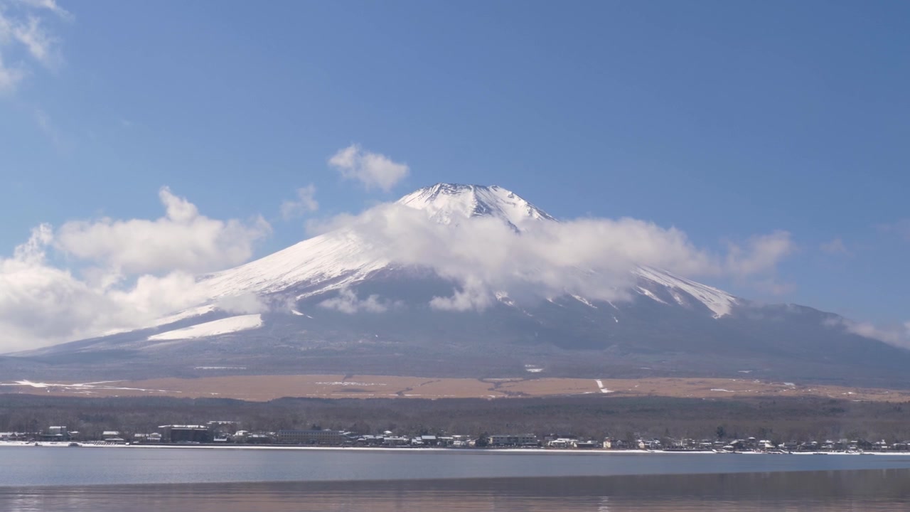日本、山梨県南都留郡の山中湖から望む、霧の雲に覆われ、国立公園の森林に囲まれた雪化粧の富士山頂のスローモーション風景。自然とランドマーク。