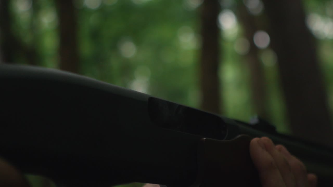 Close up of a hunter killer caucasian male hand unloading a shotgun gun outdoor forest background