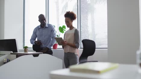 Diverse-businessman-and-businesswoman-talking,-woman-using-digital-tablet-in-office