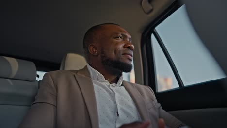 Un-Hombre-De-Negocios-Confiado-Y-Feliz-Con-Piel-Negra-Y-Traje-Marrón-Se-Despide-Por-Teléfono-Y-Mira-A-Su-Alrededor-Dentro-Del-Auto-En-Busca-De-Su-Destino.-Hombre-De-Negocios-Masculino-Con-Piel-Negra-Durante-Su-Viaje-De-Negocios.