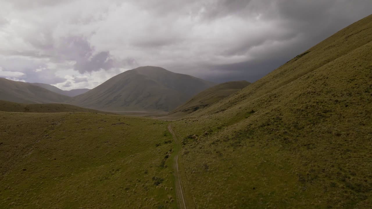 camino vacío que conduce a una línea de cresta en un desierto montañoso debajo de nubes de tormenta oscuras y pesadas