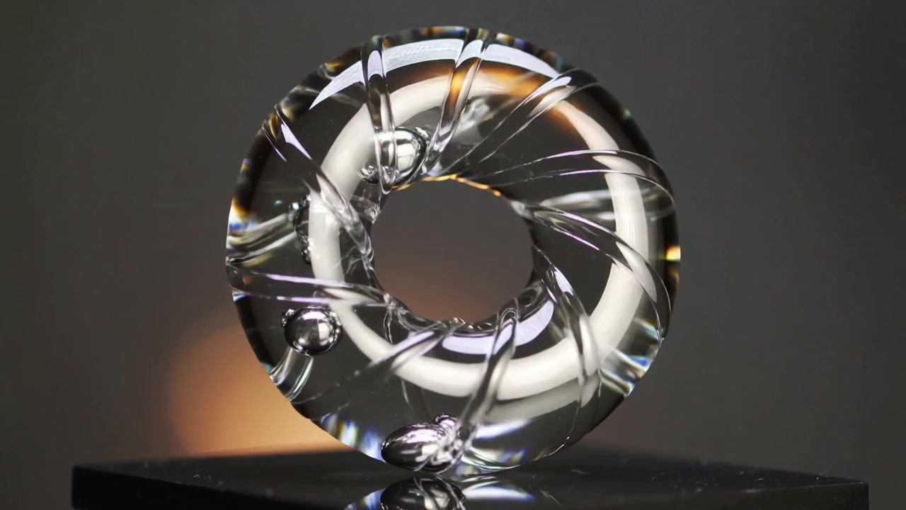 Turning platform causing clear glass torus rotating on tabletop, showing spiral grooves