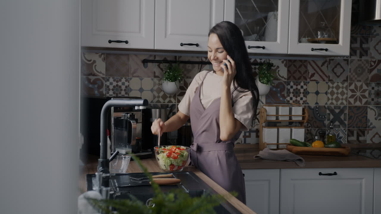 Woman Preparing Salad While Talking on the Phone in a Modern Kitchen