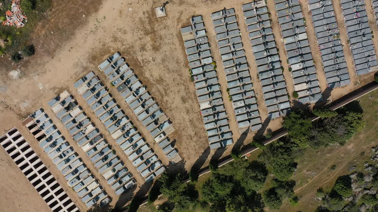 flight rising and turning over a cemetery in a rural area seeing the graves lined up forming corridors and a part with unused excavated niches there is a wall with cypresses on an afternoon Spain