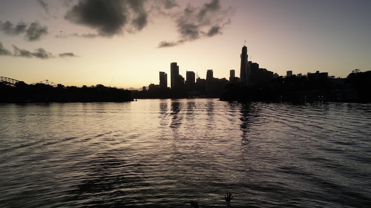 Girl standing on the edge of the water, overlooking a dark sunrise in Sydney's Harbour