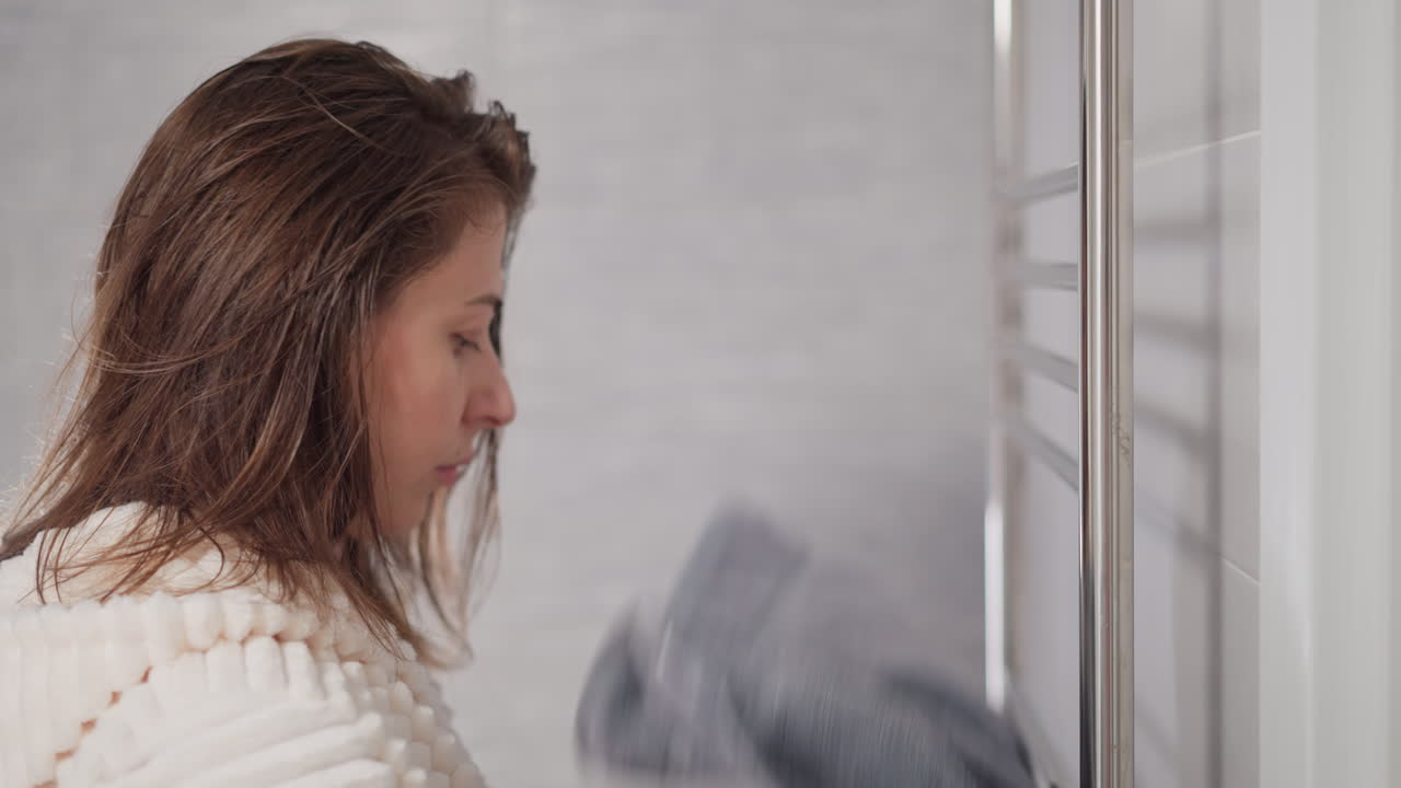 짧은 머리카락을 가진 여자가 손수건을 벗고 샤워하러 가는 느린 동작. 예쁜 여자가 신선한 깨한 손수건으로 샤워를 하고 몸을 기 위해 간다.