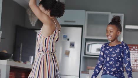 happy african american mother and daughter dancing in kitchen, slow motion