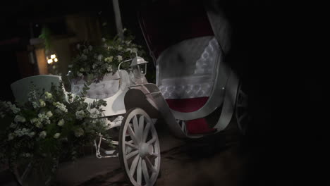 romantic white horse-drawn carriage decorated with flowers and greenery, illuminated by a lantern, creating a magical atmosphere for a wedding celebration at night, slow motion reveal