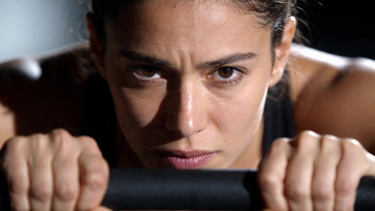 Wanita atletis memegang palang hitam, mengencangkan bahu untuk kekuatan di studio gym, mengenakan atasan hitam.