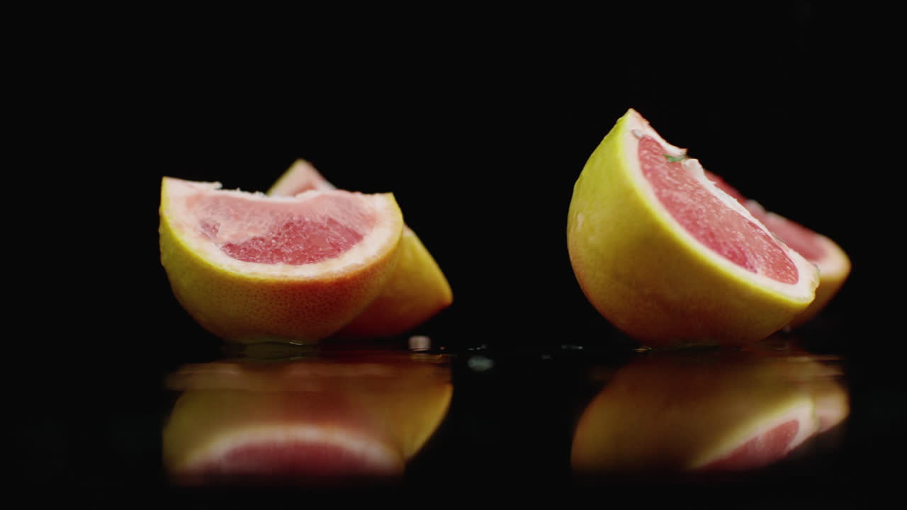 One juicy sliced ​​grapefruit falling on a glass with water splashes in slow motion on a dark background