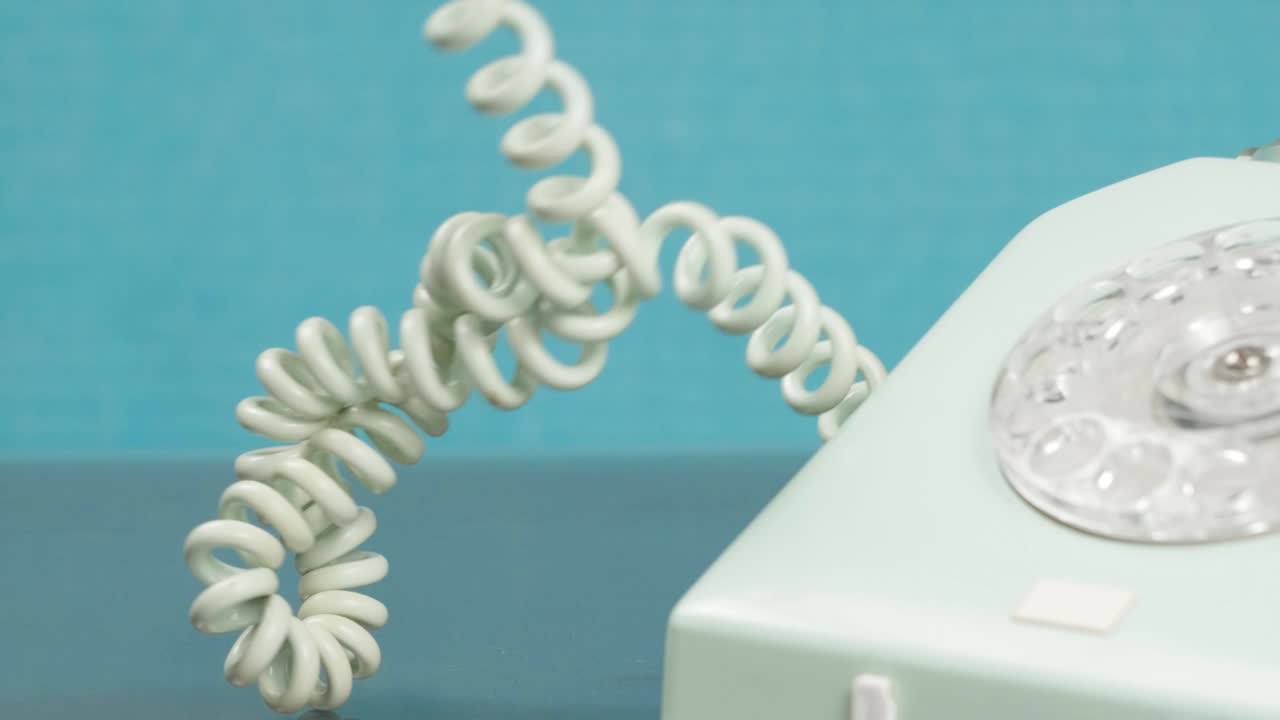 The hand unravels the cord of the old telephone. The receiver is off.