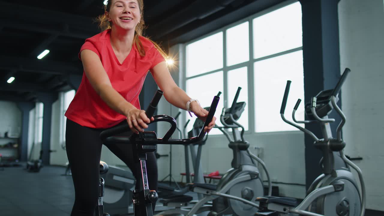 Giovane donna atletica si allena su una spin bike durante la sua routine in palestra, per la perdita di peso, al chiuso.