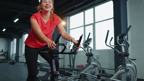 mujer joven atlética montar en bicicleta estacionaria rutina de entrenamiento en el gimnasio, pérdida de peso en el interior