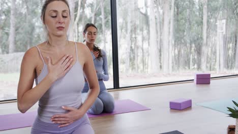 diverse women with hands on chest and stomach practicing breathing exercise on mats