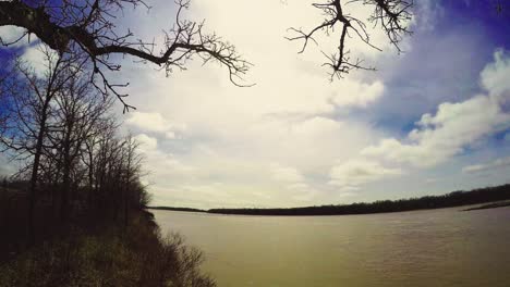 Timelapse-De-La-Orilla-Del-Río-De-Principios-De-La-Primavera-De-Dos-Niveles-De-Nubes-En-Un-Día-Soleado-Con-árboles-Y-Ramas-En-La-Orilla-Del-Río