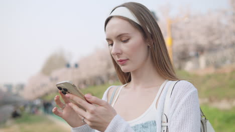 Woman-With-Long-Blonde-Hair-Using-Smartphone-At-Yangjae-Citizen's-Forest-Park-In-Seocho-District,-Seoul,-South-Korea