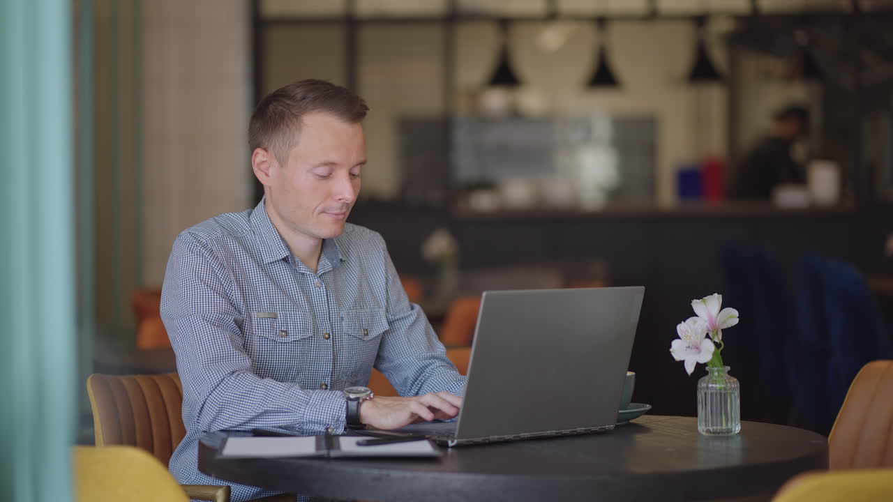A serious man is a business student working studying sitting at a table and typing a message on a laptop. Typing text on the keyboard