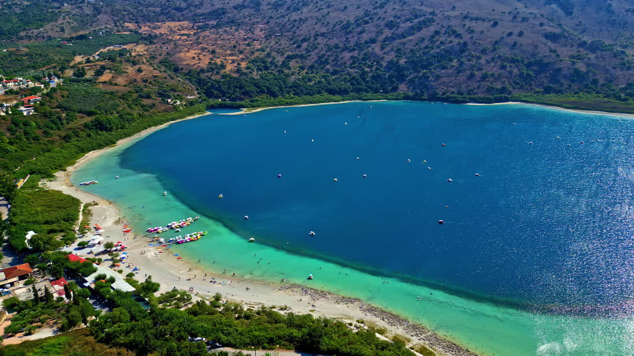 Aerial of turquoise bay with white sand beach and green hills under sunny clear skies, panoramic pullback