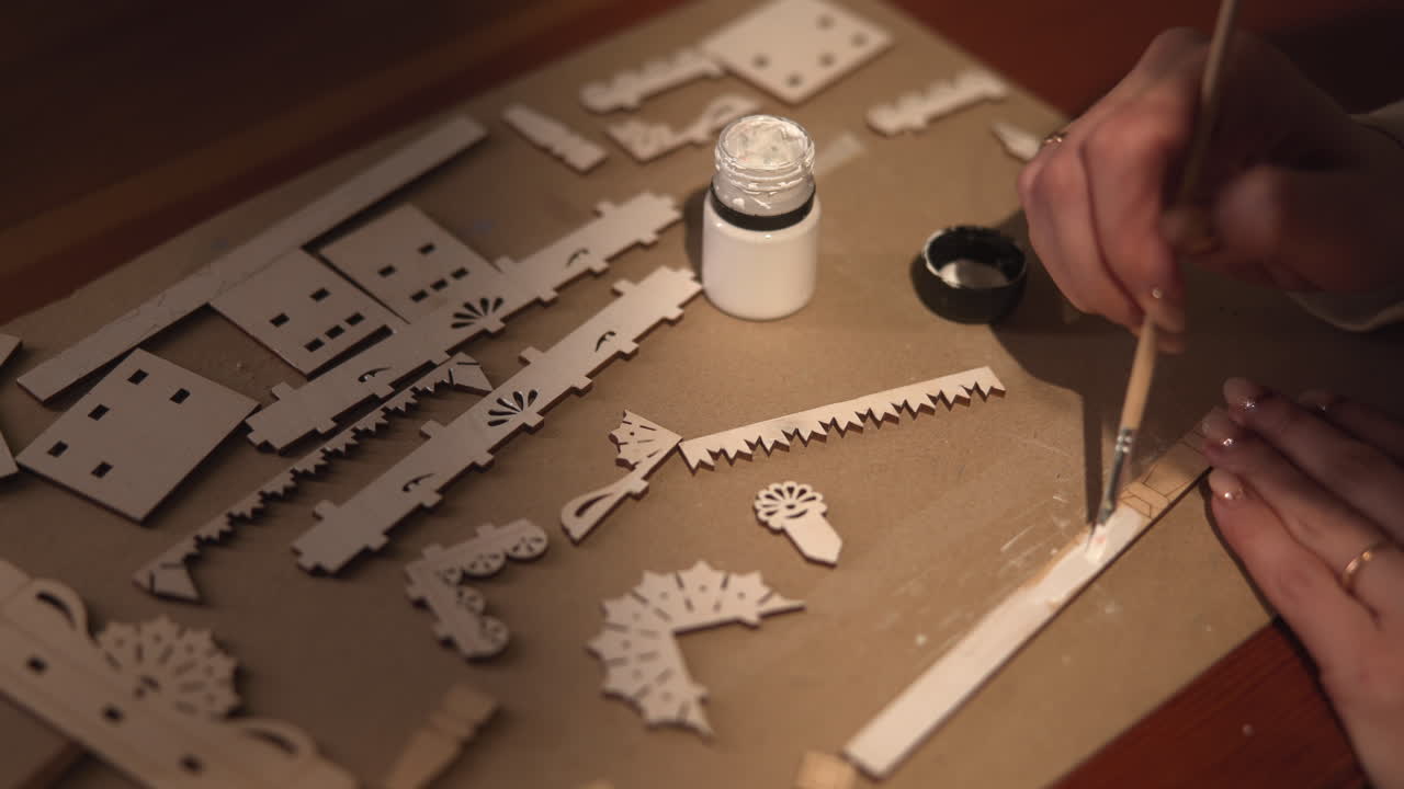 アーティストが瓶から白い絵の具を混ぜ、細長い帯に薄いウォッシュを塗る。マットには散らばったレーザー部品。