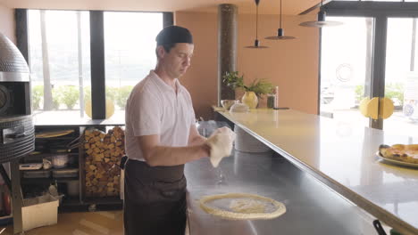 chef kneading pizza dough and waving it in the air in a restaurant kitchen