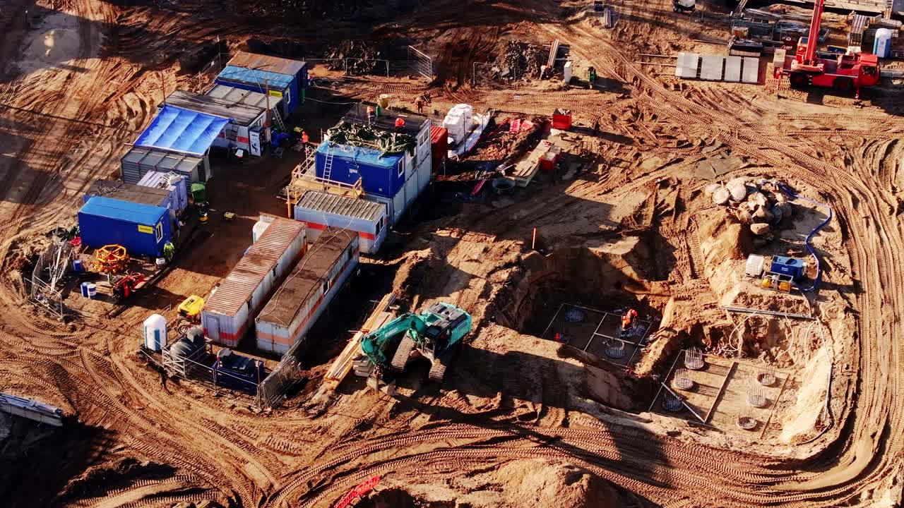 Workers and excavators operate on wide construction zone with exposed earth pits