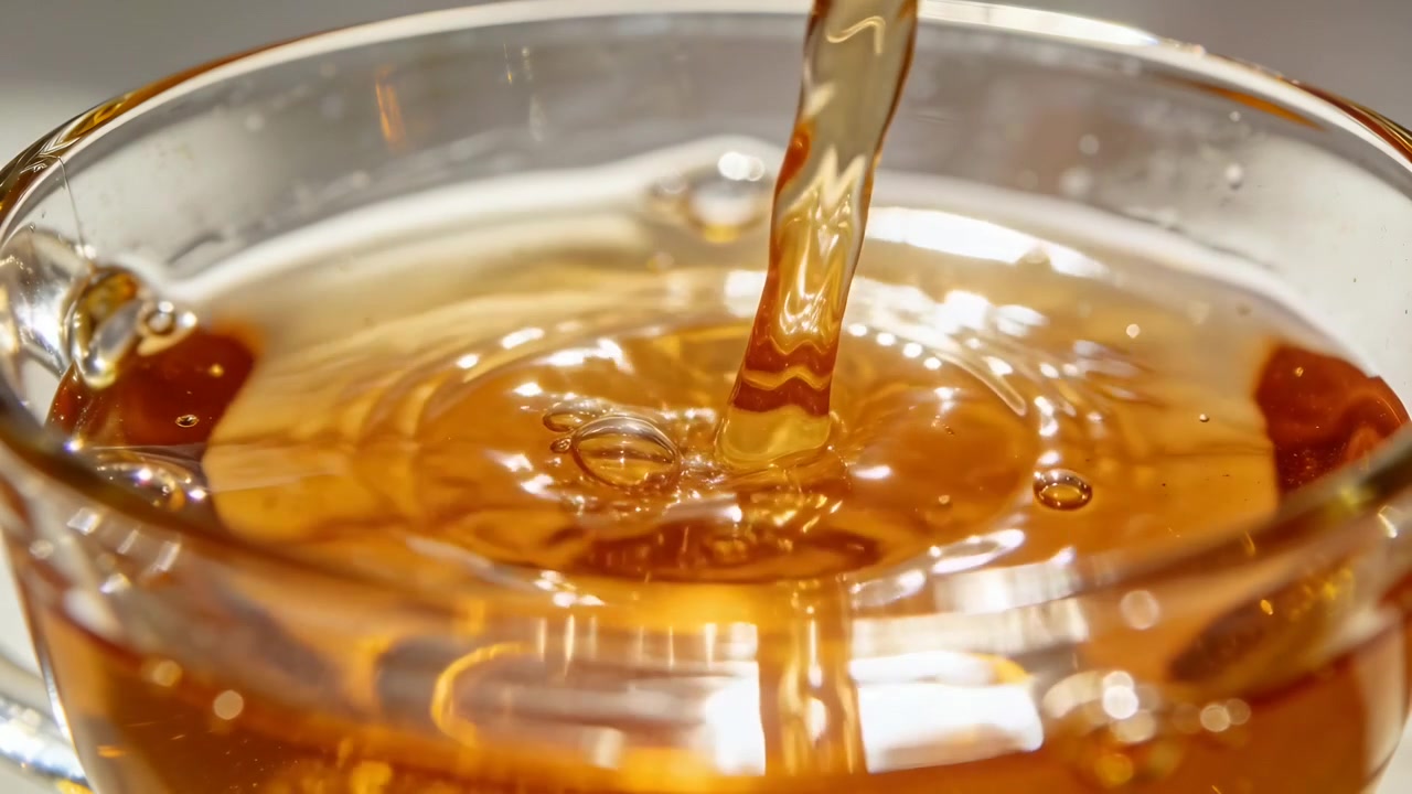 Un flusso ambrato viscoso scende, creando increspature e bolle in una tazza di vetro e riempiendo una ciotola.