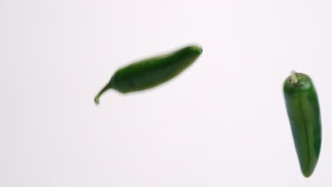 whole green jalapeños falling and bouncing in slow motion on white studio backdrop in 4k