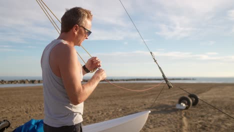 man tying knots while preparing a hobie cat on the beach