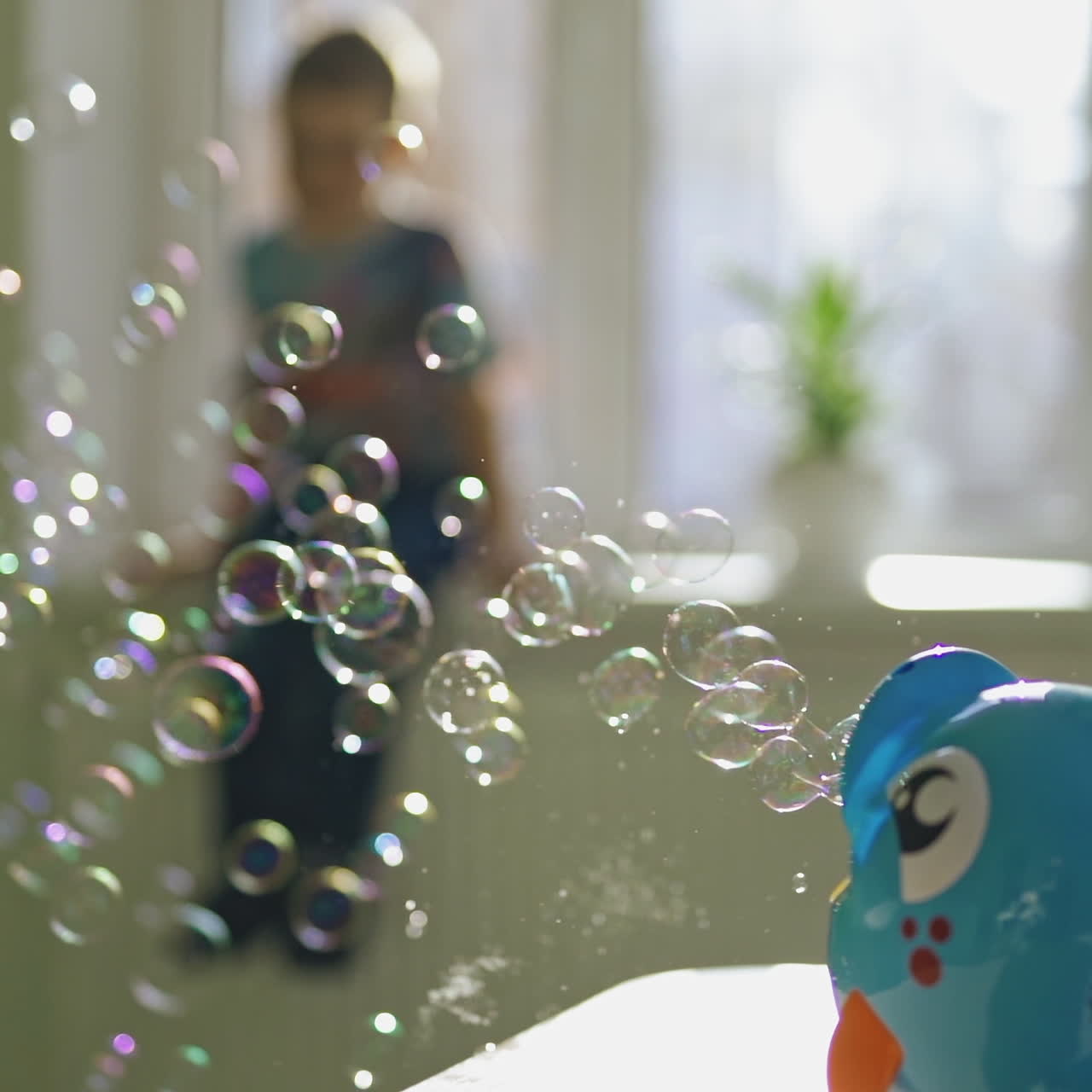 Close-up of a plastic device in a form of a fish producing soapy bubbles. Bubble blower on the table in the room with a boy who is watching at the bubbles show.