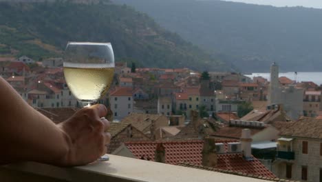 woman drinking wine on balcony with view of seaside town, komiza, croatia