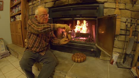 senior man is using a handmade nut cracker to open hazelnuts while sitting on fireplace hearth