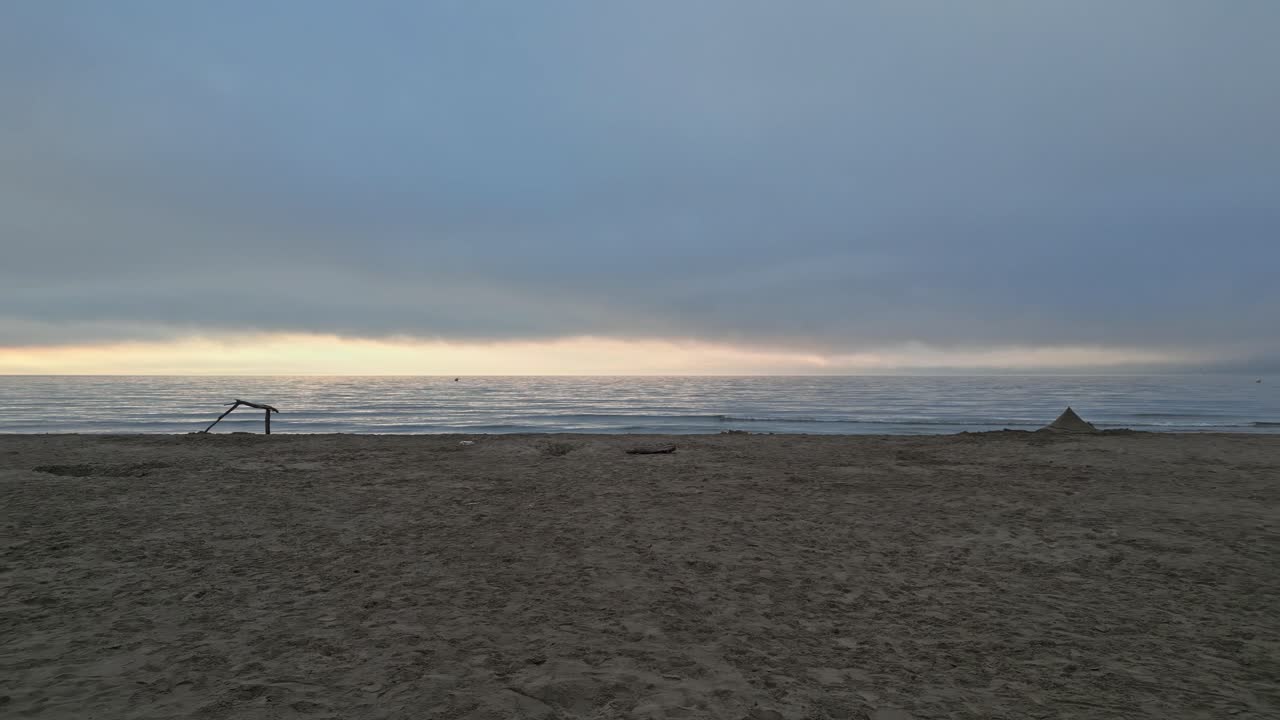 Percorrendo una spiaggia quasi deserta al tramonto. Un castello di sabbia e un pezzo di legno trasportato dalla corrente sono visibili in lontananza.