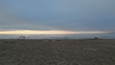 travelling along a mostly empty beach at sunset. a sandcastle and piece of driftwood are visible in the distance
