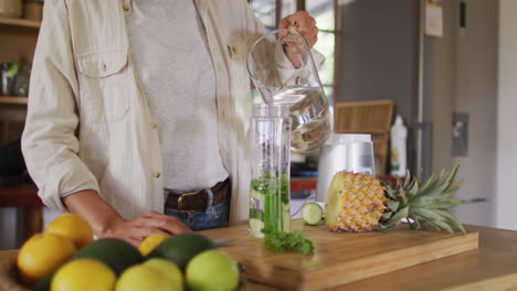 midsection of mixed race woman preparing health drink standing at counter in cottage kitchen